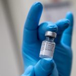 Blue gloved hand holds up Pfizer vaccine